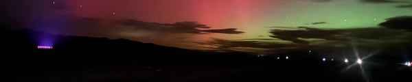 Night sky with aurora colors and greenhouse lights at Silver Lion Farms in Nevada